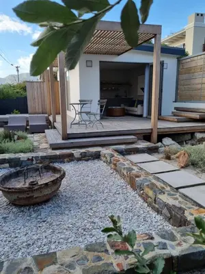a backyard with a stone walkway and a wooden deck at Potluck Cottage in Hermanus