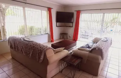 a living room with two couches and a tv at Riverside Villa in Gordonʼs Bay