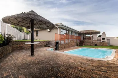 an umbrella in front of a house with a swimming pool at Cornerstone Guesthouse Alk Van Zyl in Panorama