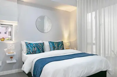 a white bedroom with a large bed with blue pillows at Century City Luxury Two Bedroom Apartment in Cape Town