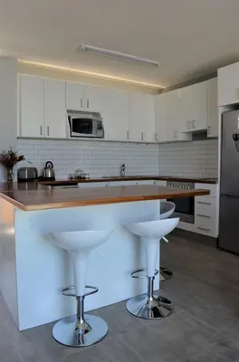 a kitchen with white cabinets and a counter with bar stools at 808 St Tropez in Cape Town