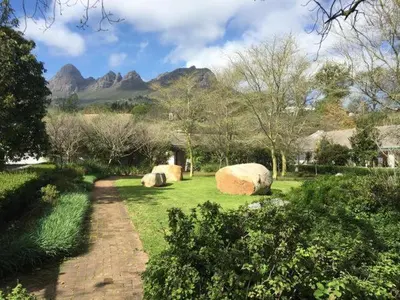 a garden with large rocks in the grass with mountains at Navarre Farm Cottages in Stellenbosch