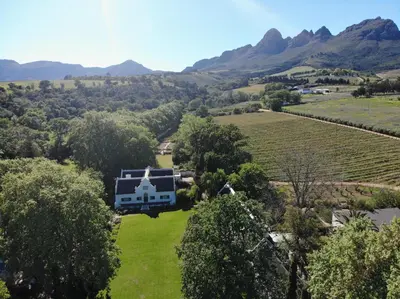 an aerial view of a house in a field with mountains at Navarre Farm Cottages in Stellenbosch