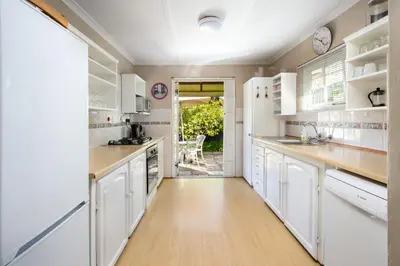 a kitchen with white cabinets and a wooden floor at Quainton Cottages in Hermanus