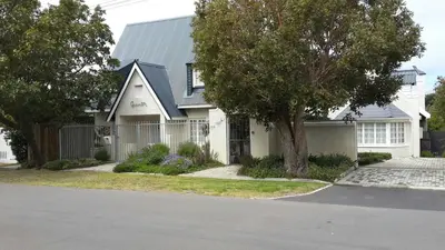 a white house with a tree and a driveway at Quainton Cottages in Hermanus