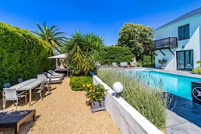 a pool with tables and chairs next to a house at La Bonne Auberge in Somerset West