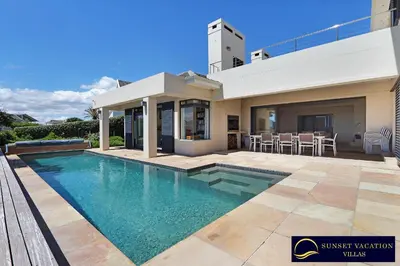 a swimming pool in front of a house at Kite Surfers Beach Villa in Cape Town