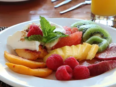 a white plate of fruit with whipped cream and strawberries at The Yacht in Hermanus