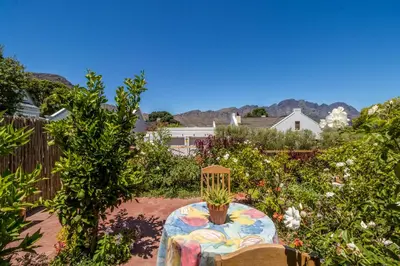 a garden with a table and chairs and flowers at Protea Room Franschhoek Central in Franschhoek