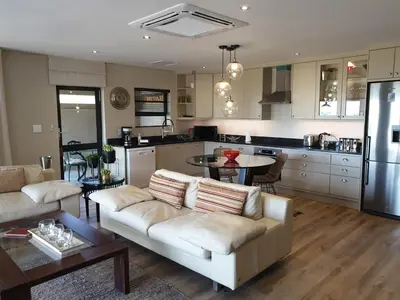 a living room with a white couch and a kitchen at Vrede Selfcatering in Somerset West