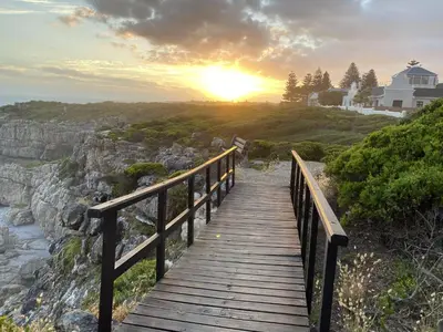 a wooden boardwalk leading to a beach with the sunset at Hermanus 60 on Flat in Hermanus