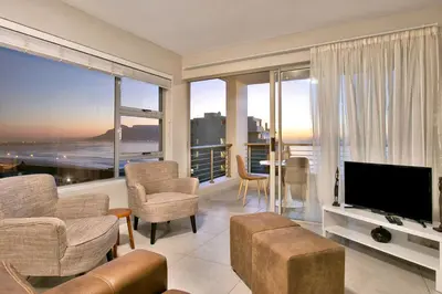 a living room with a tv and a couch and chairs at Ocean View A603 in Cape Town