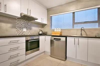 a kitchen with white cabinets and a stainless steel dishwasher at Ocean View A603 in Cape Town