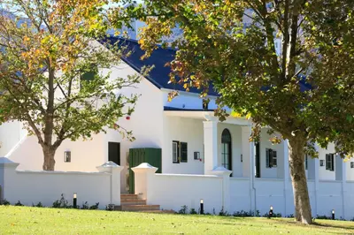 a white house with trees in the foreground at La Cotte The Manor House in Franschhoek