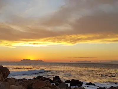a sunset over the ocean with rocks on the beach at Kleinblom in Pringle in Pringle Bay