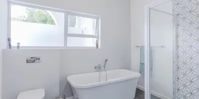 a white bathroom with a tub and a toilet and a window at The Views Guesthouse in Somerset West