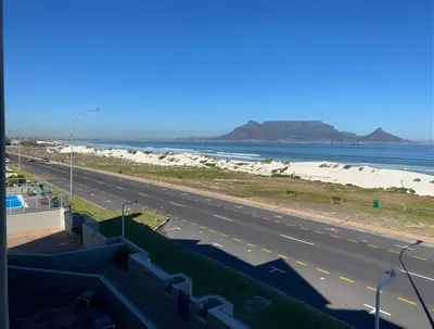 a highway next to a beach and the ocean at On The Beach Front Sea Spray in Bloubergstrand