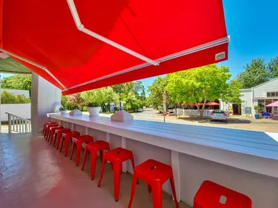 a bar with red stools and a red umbrella at The Post House Hotel - no children under the age of 16yrs in Greyton