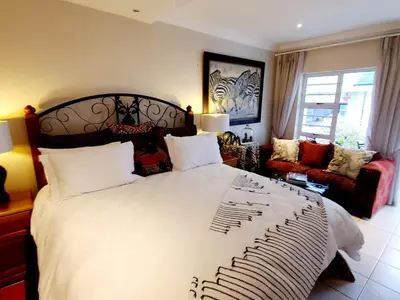 a bedroom with a large bed and a living room at Gordon's Beach Lodge in Gordonʼs Bay