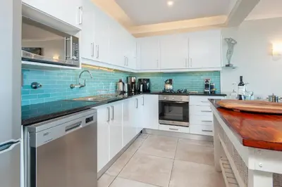 a kitchen with white cabinets and blue tiles at Walker Bay Luxury Seafront Apartment in Hermanus