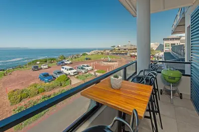 a table on a balcony with a view of the ocean at Walker Bay Luxury Seafront Apartment in Hermanus