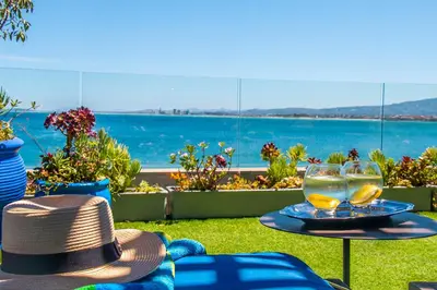 a hat and two glasses on a table with a view of the ocean at 185 on BEACH Boutique Suites in Gordonʼs Bay