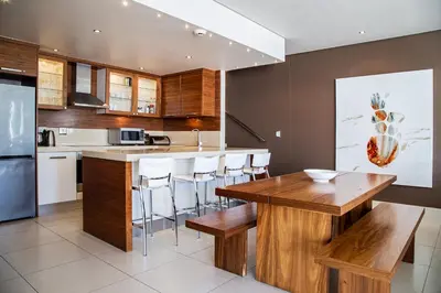 a kitchen with a wooden table and bar with stools at Marine Square Luxury Suites in Hermanus