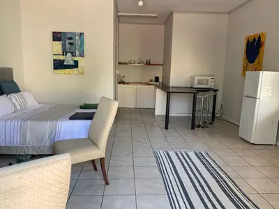 a bedroom with a bed and a table and a refrigerator at Le Grec Wine Tram Apartment #1 in Franschhoek