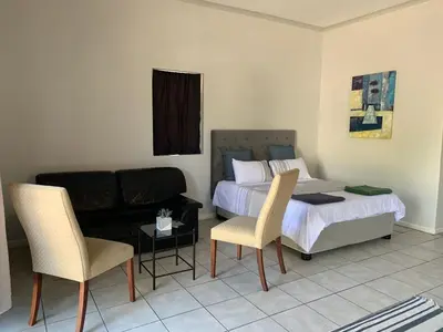 a bedroom with a bed and a couch and chairs at Le Grec Wine Tram Apartment #1 in Franschhoek