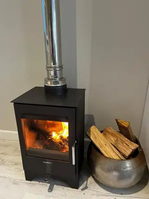 a black stove sitting next to a bowl of wood at Modern Spacious Cottage with Hot Tub, Flora Studio in Hermanus