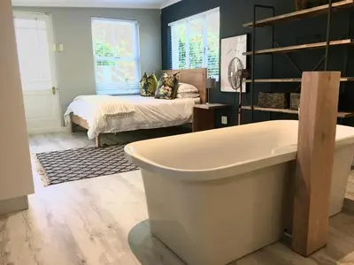 a bathroom with a tub and a bed in a room at Modern Spacious Cottage with Hot Tub, Flora Studio in Hermanus