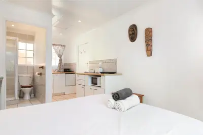 a white bedroom with a large bed and a kitchen at The Bohemian Guesthouse in Cape Town