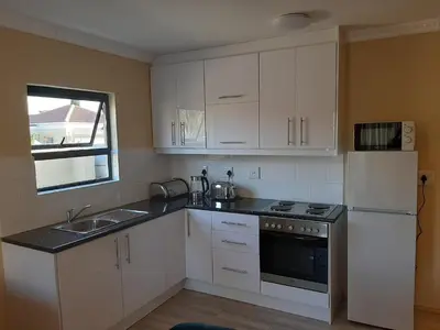 a kitchen with white cabinets and a sink and a refrigerator at Shalom Self catering in Cape Town