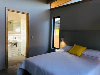 a bedroom with a bed and a bathroom with a sink at Palm and Pine Cottage in Cape Town