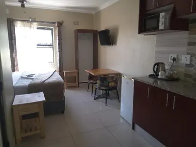 a room with a bed and a kitchen with a table at Victoria Guest Lodge in Bellville
