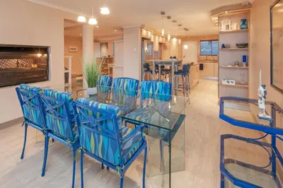 a dining room with a glass table and blue chairs at Hermanus Haven, entire home, on the sea, private pool, secure in Hermanus