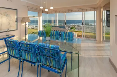 a dining room with a glass table and blue chairs at Hermanus Haven, entire home, on the sea, private pool, secure in Hermanus