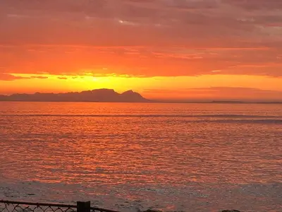 a sunset over the ocean with mountains in the distance at By Die See in Gordonʼs Bay