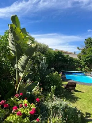 a garden with a pool and a bench and flowers at Sunset Beach Living Guesthouse in Cape Town