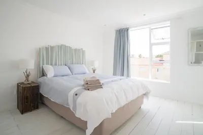 a white bedroom with a large bed and a window at Sunset Beach Living Guesthouse in Cape Town