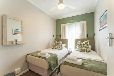 a room with two beds and a mirror and a window at Fairway Holiday Accommodation in Hermanus