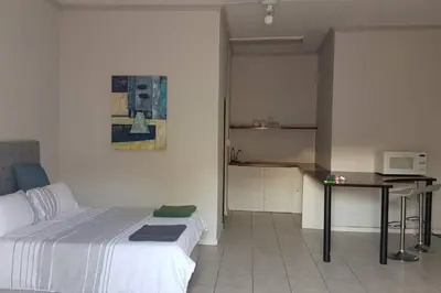 a bedroom with a bed and a table and a kitchen at Le Grec Wine Tram Apartment #3 in Franschhoek