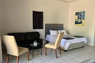 a bedroom with a bed and a couch and chairs at Le Grec Wine Tram Apartment #3 in Franschhoek