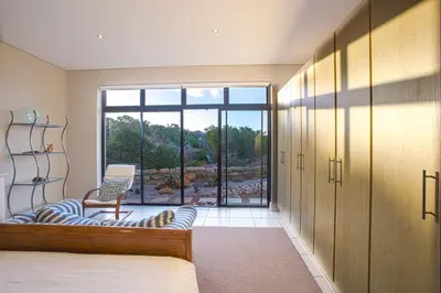 a bedroom with a bed and a chair and a window at Gecko House in Pringle Bay