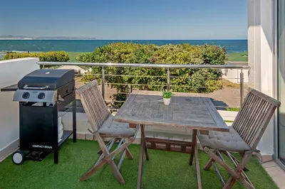 a table and chairs on a balcony with a grill at 64 Whalerock Estate in Hermanus