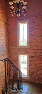 a staircase in a brick room with a chandelier and two windows at Sandmartins Private Secure Villa in Simondium