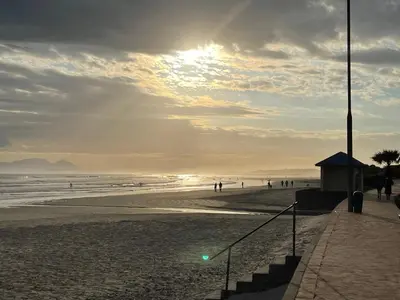 a beach with people walking on the sand and the ocean at Jackie’s 3 bedroomed secure beach front apartment Strand Golden Mile in Strand