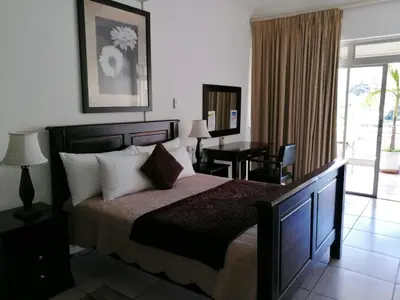 a bedroom with a bed and a desk and a window at Sunset Boulevard Riverlodge in Paarl