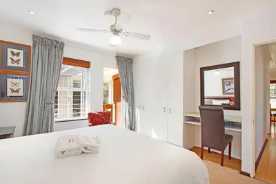 a white bedroom with a bed and a chair at Kwantu Guesthouse 1 in Cape Town