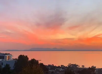 a sunset over a body of water with a city at On the GBay Villa in Gordonʼs Bay